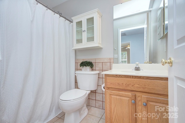 bathroom with tile patterned floors, tile walls, toilet, vanity, and a wainscoted wall