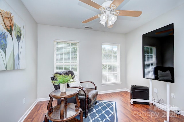 living area featuring wood finished floors, a ceiling fan, and baseboards