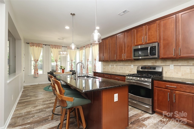10217 Falling Leaf Dr, Concord, NC 28027 - kitchen featuring appliances with stainless steel finishes, a sink, backsplash, dark stone countertops, and a center island with sink