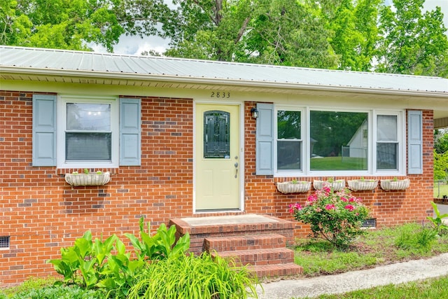 view of front of home with brick siding, metal roof, and crawl space