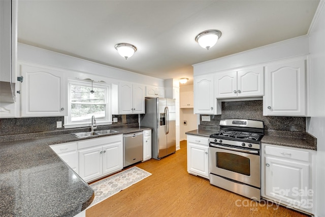 kitchen with stainless steel appliances, a sink, dark countertops, light wood-style floors, and white cabinetry