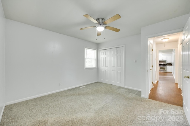 unfurnished bedroom featuring attic access, carpet flooring, baseboards, a closet, and a ceiling fan