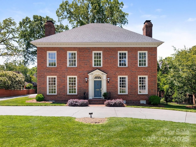 colonial inspired home featuring a chimney, brick siding, roof with shingles, and crawl space