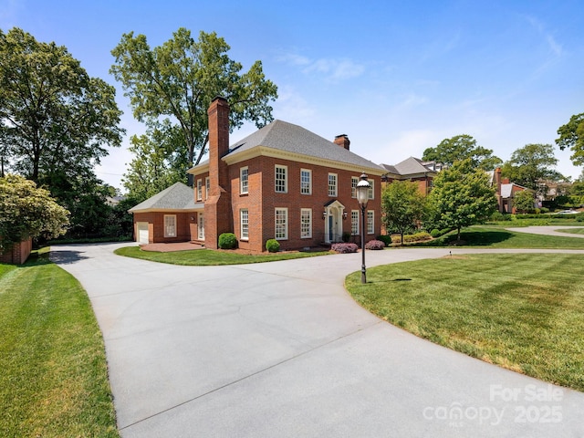 colonial house with a chimney, curved driveway, a front lawn, and brick siding