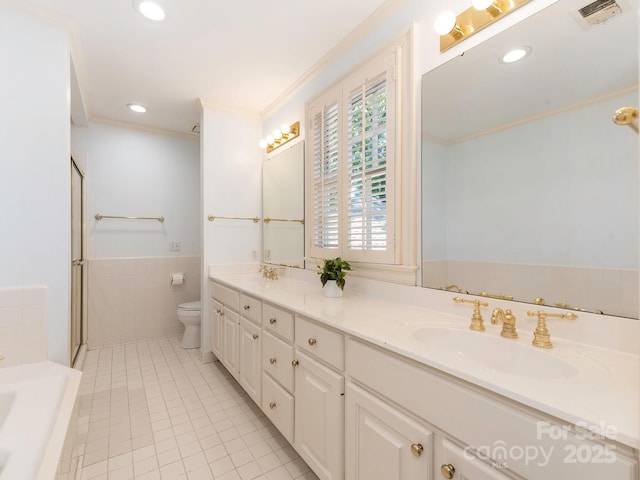 bathroom with tile patterned floors, toilet, crown molding, double vanity, and tile walls