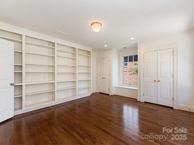 unfurnished bedroom featuring two closets, ornamental molding, wood finished floors, baseboards, and recessed lighting