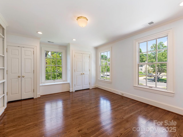 unfurnished bedroom with two closets, crown molding, wood finished floors, baseboards, and recessed lighting