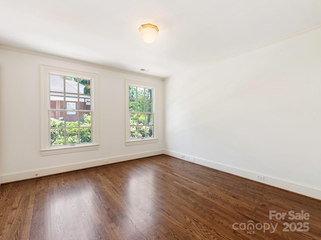 spare room featuring healthy amount of natural light, baseboards, dark wood-style floors, and crown molding