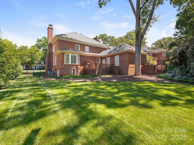 rear view of property featuring a chimney, brick siding, a deck, and a lawn