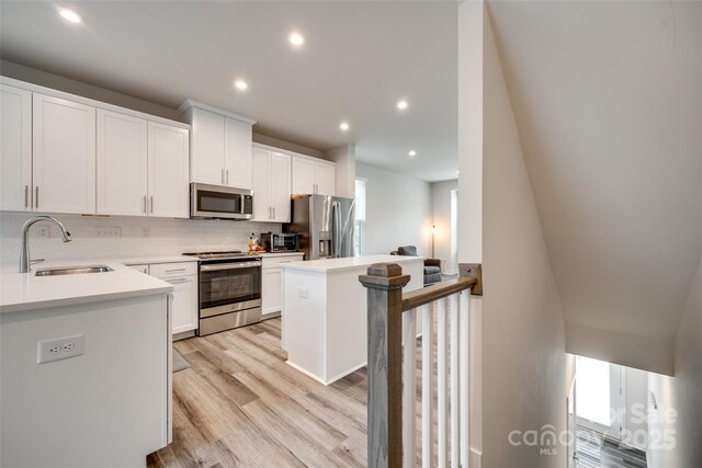 kitchen featuring stainless steel appliances, a sink, decorative backsplash, light wood-type flooring, and light countertops
