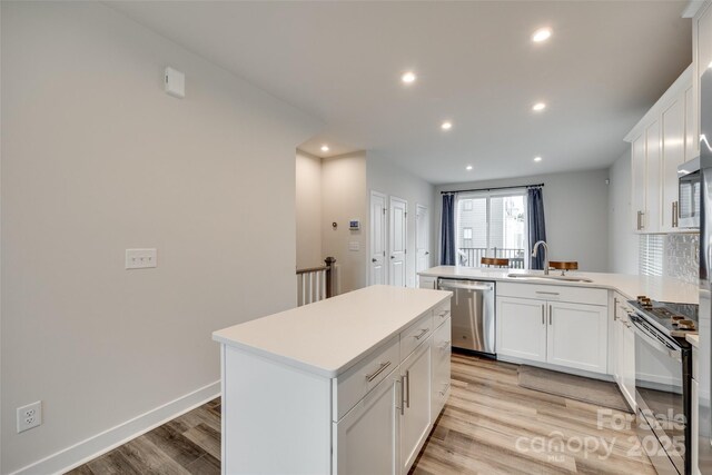 kitchen featuring appliances with stainless steel finishes, a sink, light wood finished floors, a peninsula, and recessed lighting