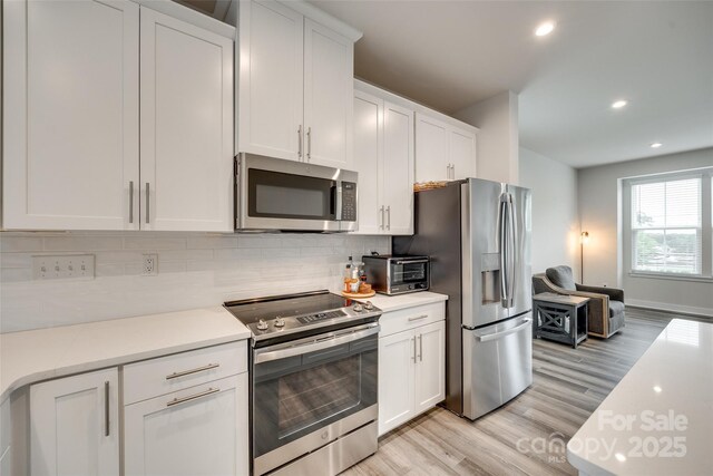 kitchen with appliances with stainless steel finishes, light wood-type flooring, white cabinetry, decorative backsplash, and light countertops