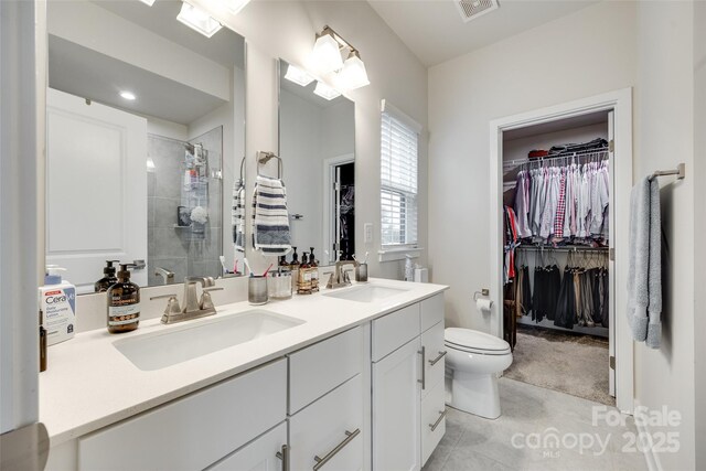 bathroom featuring a shower stall, a walk in closet, double vanity, toilet, and tile patterned flooring