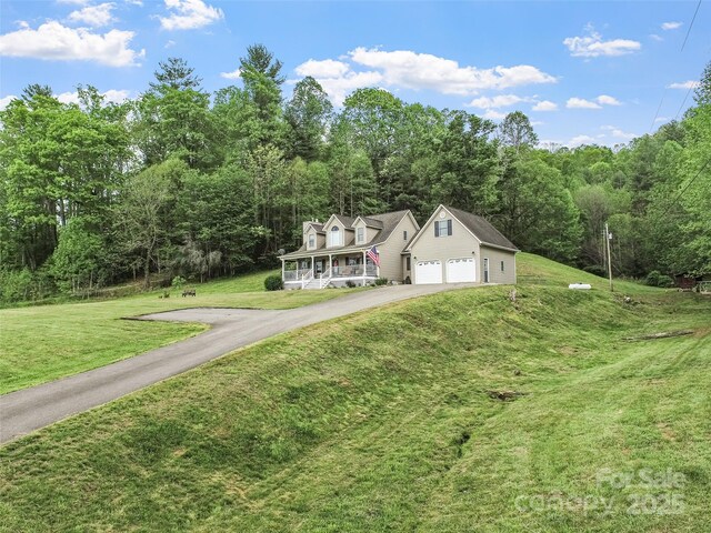 view of front of home with a front lawn, driveway, a forest view, and a garage