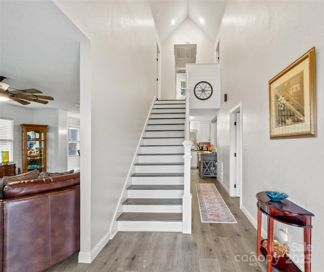 stairway featuring baseboards, wood finished floors, a ceiling fan, and high vaulted ceiling