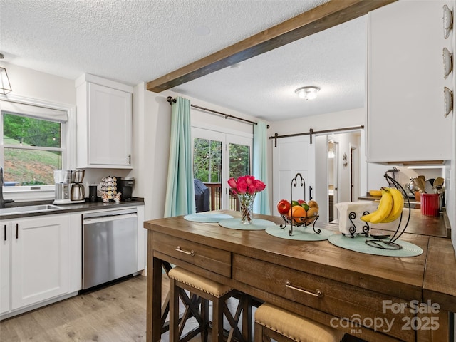 kitchen with a textured ceiling, a sink, white cabinets, and stainless steel dishwasher