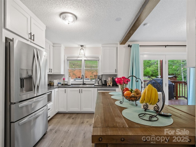 kitchen featuring a textured ceiling, stainless steel fridge, white cabinetry, and a sink