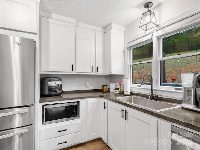 kitchen with a textured ceiling, white cabinetry, stainless steel appliances, and a sink