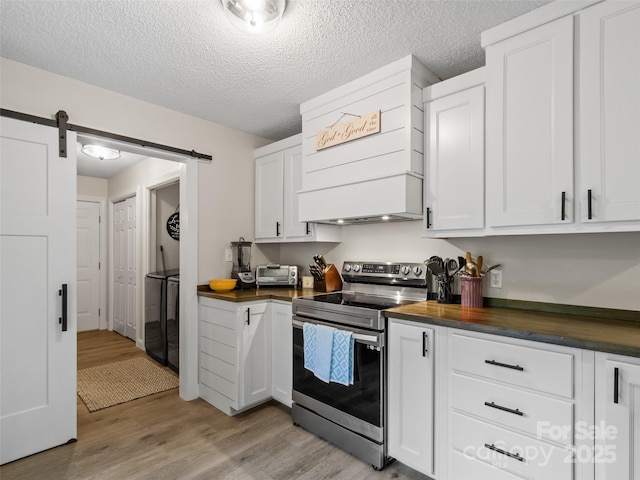 kitchen featuring stacked washing maching and dryer, electric range, light wood-type flooring, butcher block counters, and custom exhaust hood
