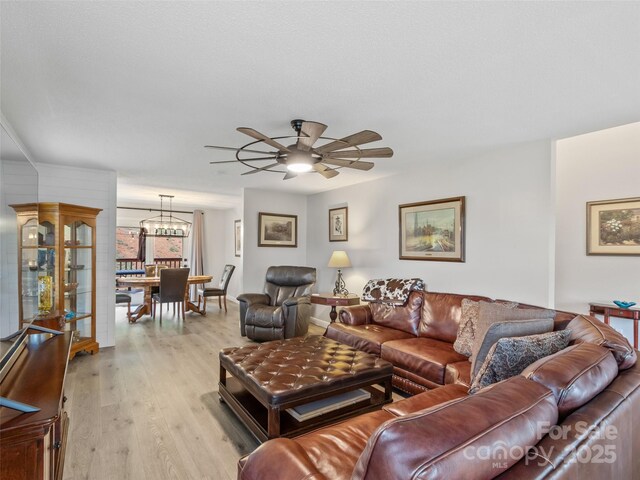 living room with light wood-style floors and ceiling fan with notable chandelier