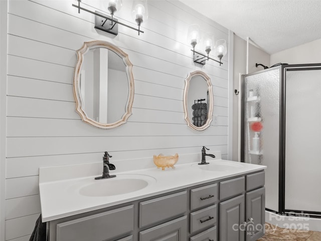 bathroom with double vanity, a textured ceiling, a shower stall, and a sink