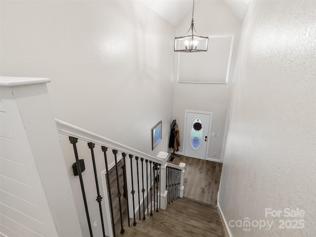 stairs featuring vaulted ceiling, an inviting chandelier, and wood finished floors
