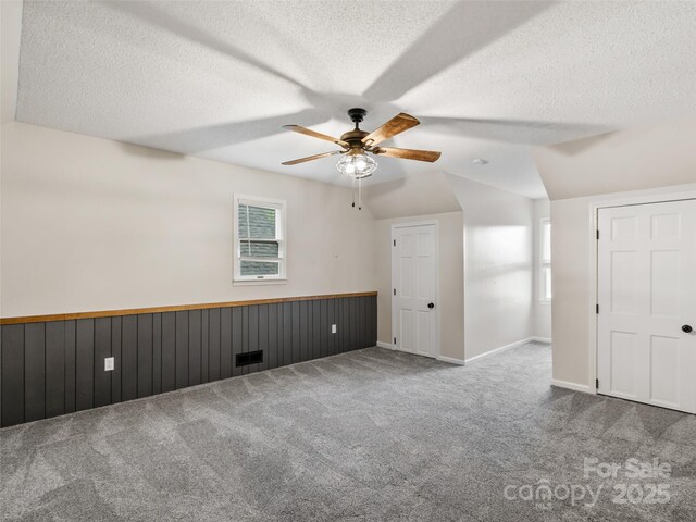 interior space featuring carpet flooring, multiple windows, a textured ceiling, and vaulted ceiling