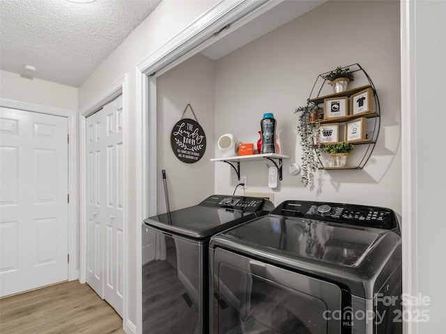 washroom with laundry area, light wood-style floors, washing machine and dryer, and a textured ceiling