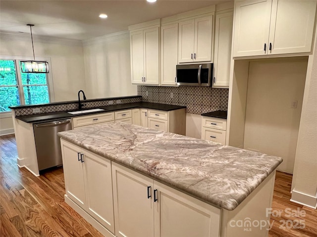 kitchen featuring appliances with stainless steel finishes, a sink, a peninsula, wood finished floors, and white cabinetry