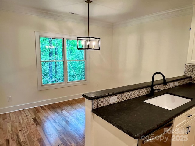 kitchen featuring a sink, white cabinetry, crown molding, wood finished floors, and a chandelier
