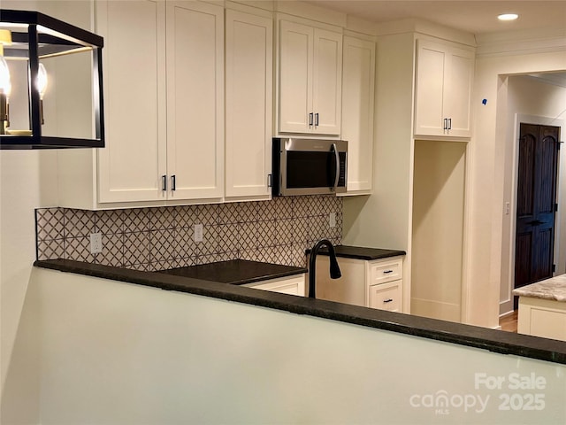kitchen with stainless steel microwave, backsplash, white cabinetry, recessed lighting, and dark countertops