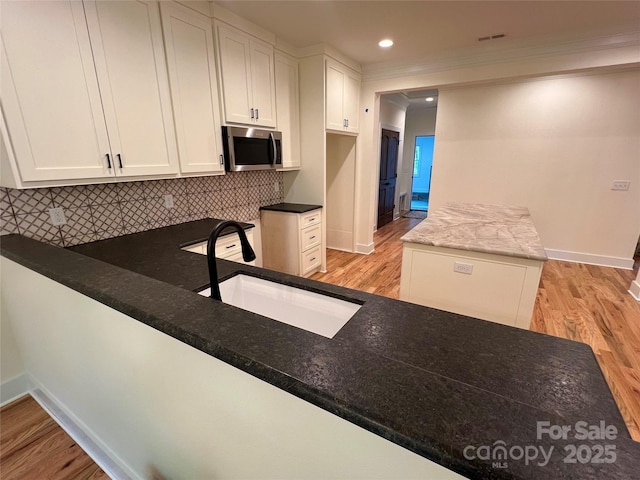 kitchen featuring stainless steel microwave, ornamental molding, baseboards, backsplash, and white cabinetry