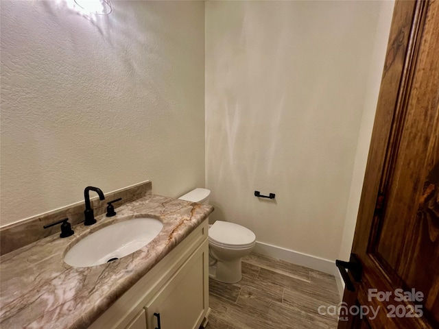 bathroom featuring vanity, toilet, baseboards, a textured wall, and wood finished floors