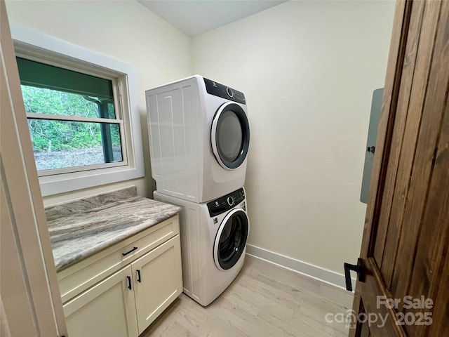 laundry area featuring stacked washer and clothes dryer, cabinet space, baseboards, and light wood finished floors