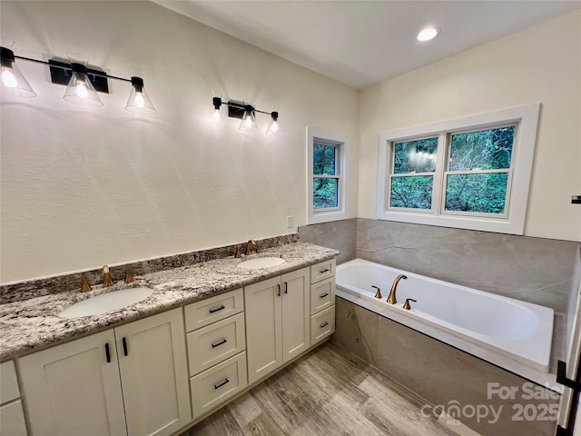 full bath with wood finished floors, a garden tub, and double vanity