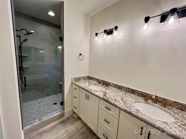 full bathroom featuring a shower stall, wood finished floors, double vanity, and baseboards