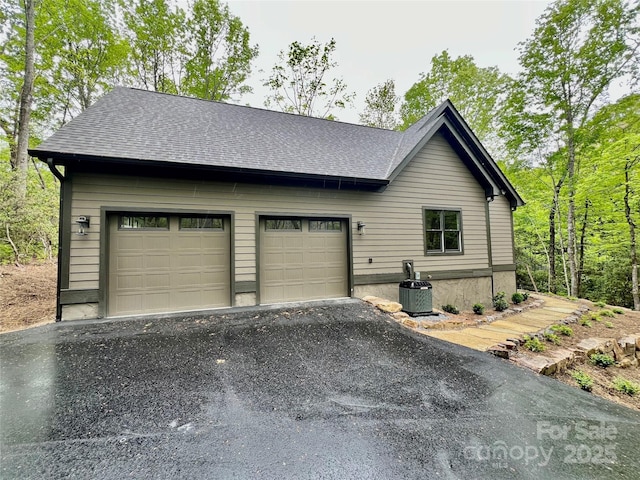 view of home's exterior with asphalt driveway, a shingled roof, central AC, and an attached garage