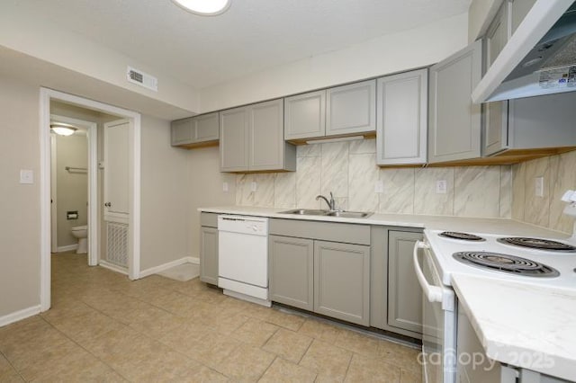 kitchen with gray cabinetry, under cabinet range hood, white appliances, a sink, and light countertops