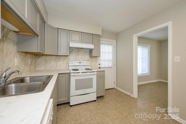 kitchen with white electric range oven, gray cabinets, a sink, under cabinet range hood, and tasteful backsplash