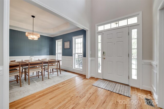 entryway with wood finished floors, a chandelier, wainscoting, crown molding, and healthy amount of natural light