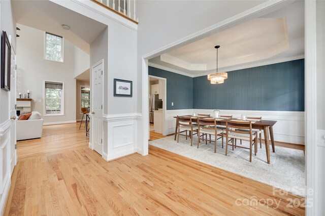 dining area with healthy amount of natural light, wood finished floors, crown molding, a wainscoted wall, and a tray ceiling