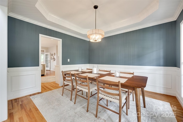 dining space featuring a wainscoted wall, wood finished floors, ornamental molding, a chandelier, and a tray ceiling