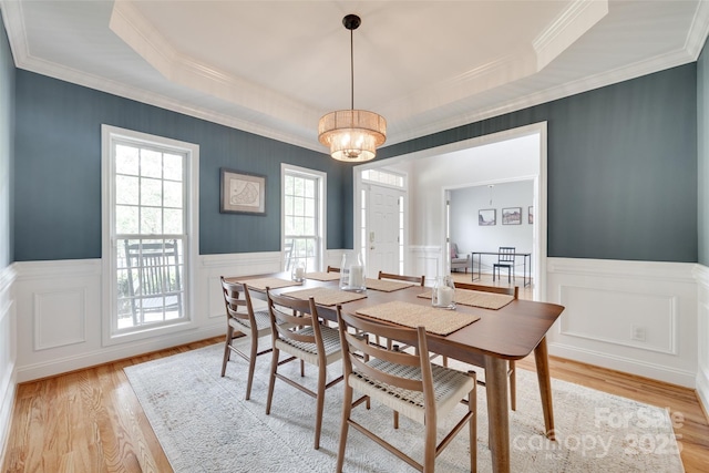dining room with a wainscoted wall, light wood-style floors, a tray ceiling, crown molding, and a decorative wall