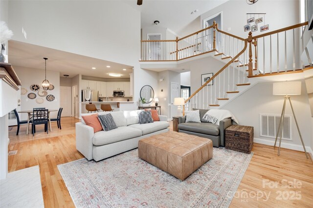 living room with stairs, light wood-style floors, a high ceiling, a chandelier, and baseboards
