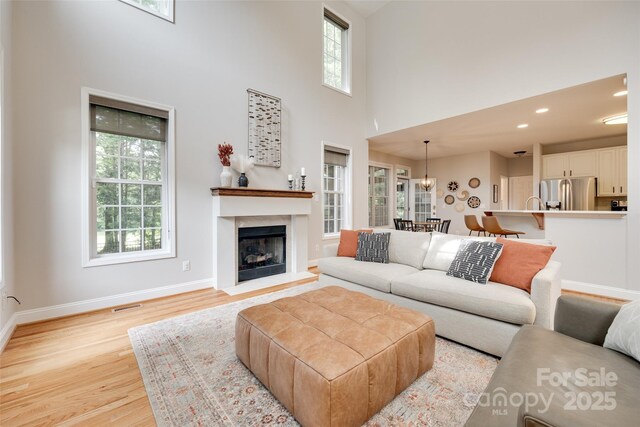 living room with plenty of natural light, light wood finished floors, a high ceiling, baseboards, and a fireplace with raised hearth