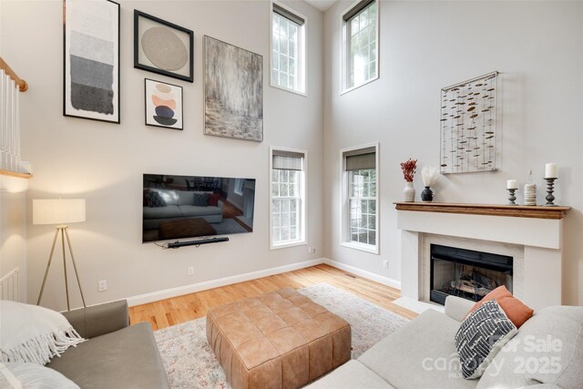 living room featuring healthy amount of natural light, wood finished floors, a fireplace with flush hearth, baseboards, and a high ceiling
