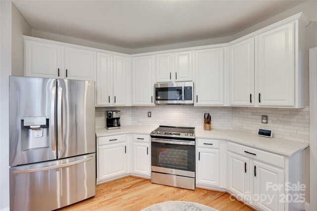 kitchen with stainless steel appliances, light wood-style floors, white cabinetry, and decorative backsplash