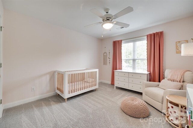 bedroom with a crib, carpet floors, baseboards, and ceiling fan