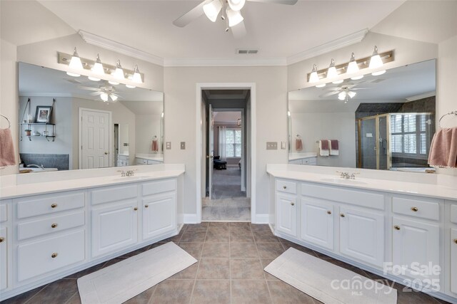 bathroom featuring ceiling fan, a shower stall, two vanities, and ornamental molding