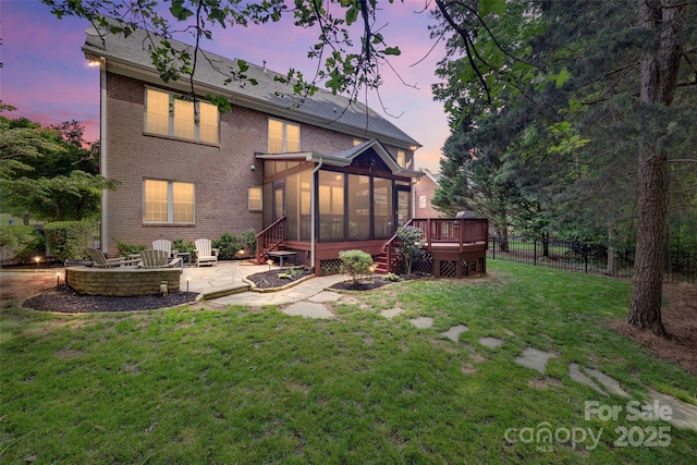 rear view of house featuring a sunroom, a patio area, brick siding, a fire pit, and a deck